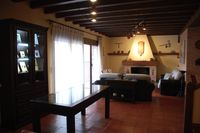Salón de la casa rural La Fuente Gorda: chimenea y ventanal al fondo, mesa y vitrina expositora a la izquierda.